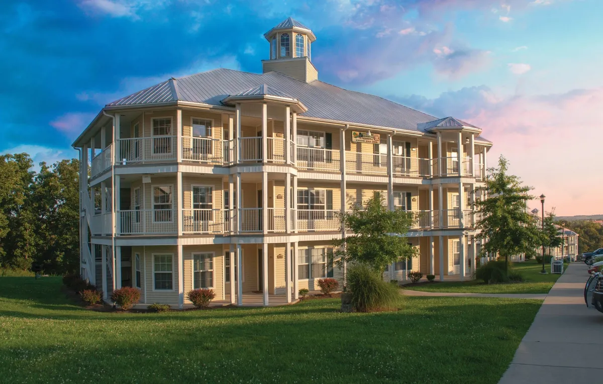The exterior of a three-story villa complex, with inviting balconies overlooking a meticulously landscaped lawn. The warm hues of the sunset sky create a tranquil backdrop, while the balconies hint at the private comfort and year-round enjoyment available to guests.