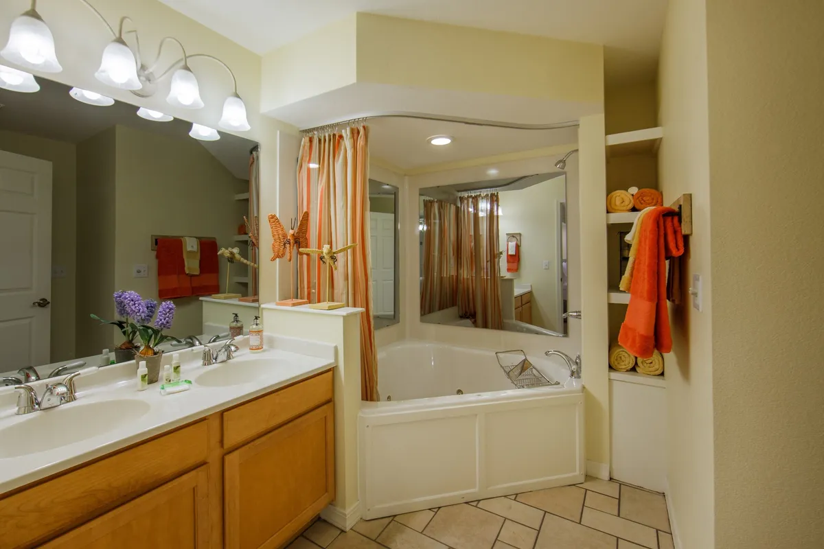 A modern bathroom featuring a double sink vanity, a comfortable bathtub, colorful towels, and a large mirror. The space feels calm, clean, and thoughtfully designed for relaxation and efficient morning routines.