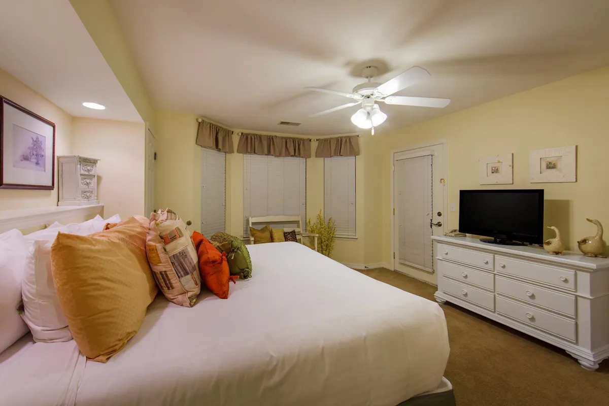 A serene bedroom scene featuring a comfortable bed adorned with decorative pillows, a sleek dresser, and a wall-mounted television. The space is softly lit and designed for relaxation, inviting guests to unwind, read, or enjoy a quiet morning in bed.